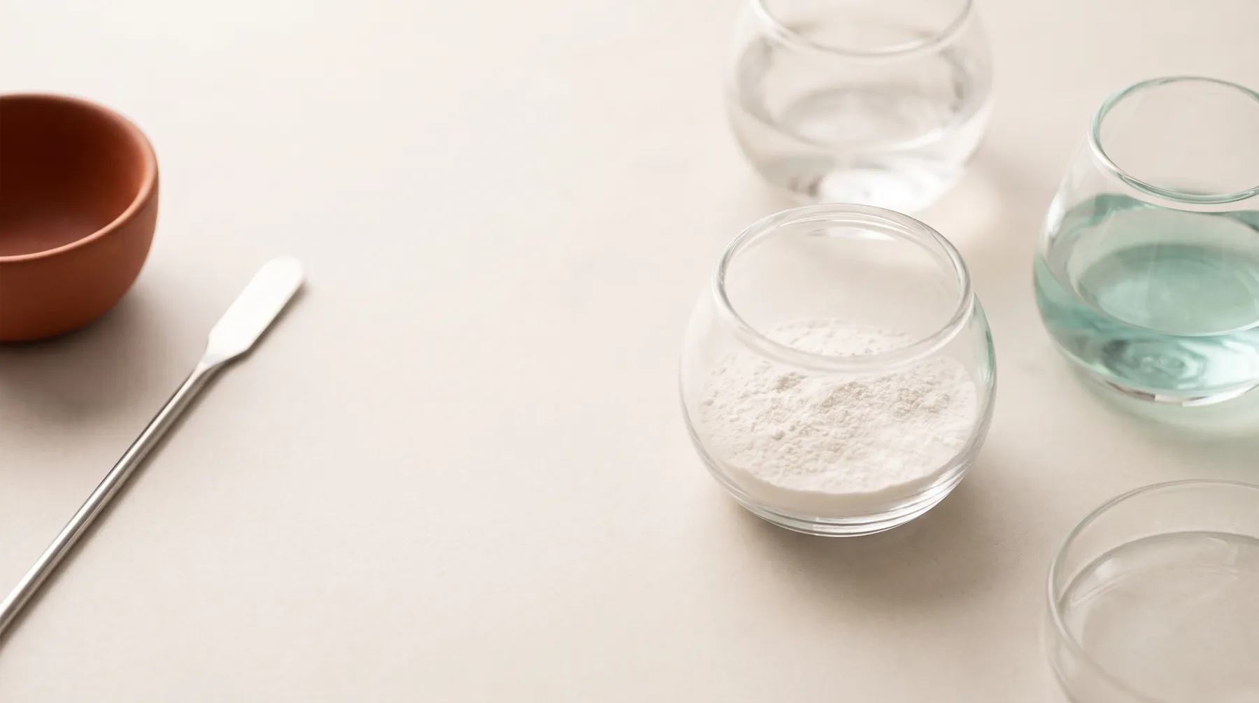 Glass vessels with fine white powder and pale teal liquid beside a steel spatula